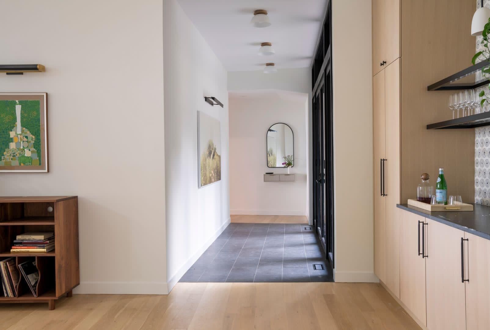 Modern hallway with light wood floors, white walls, built-in shelving, and a cabinet with decor accents.