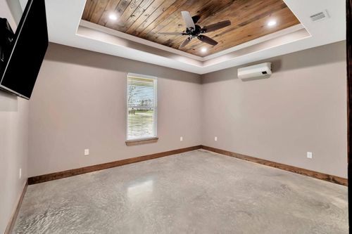 Empty beige bedroom with carpet, wood ceiling, ceiling fan, window, and wall-mounted AC unit