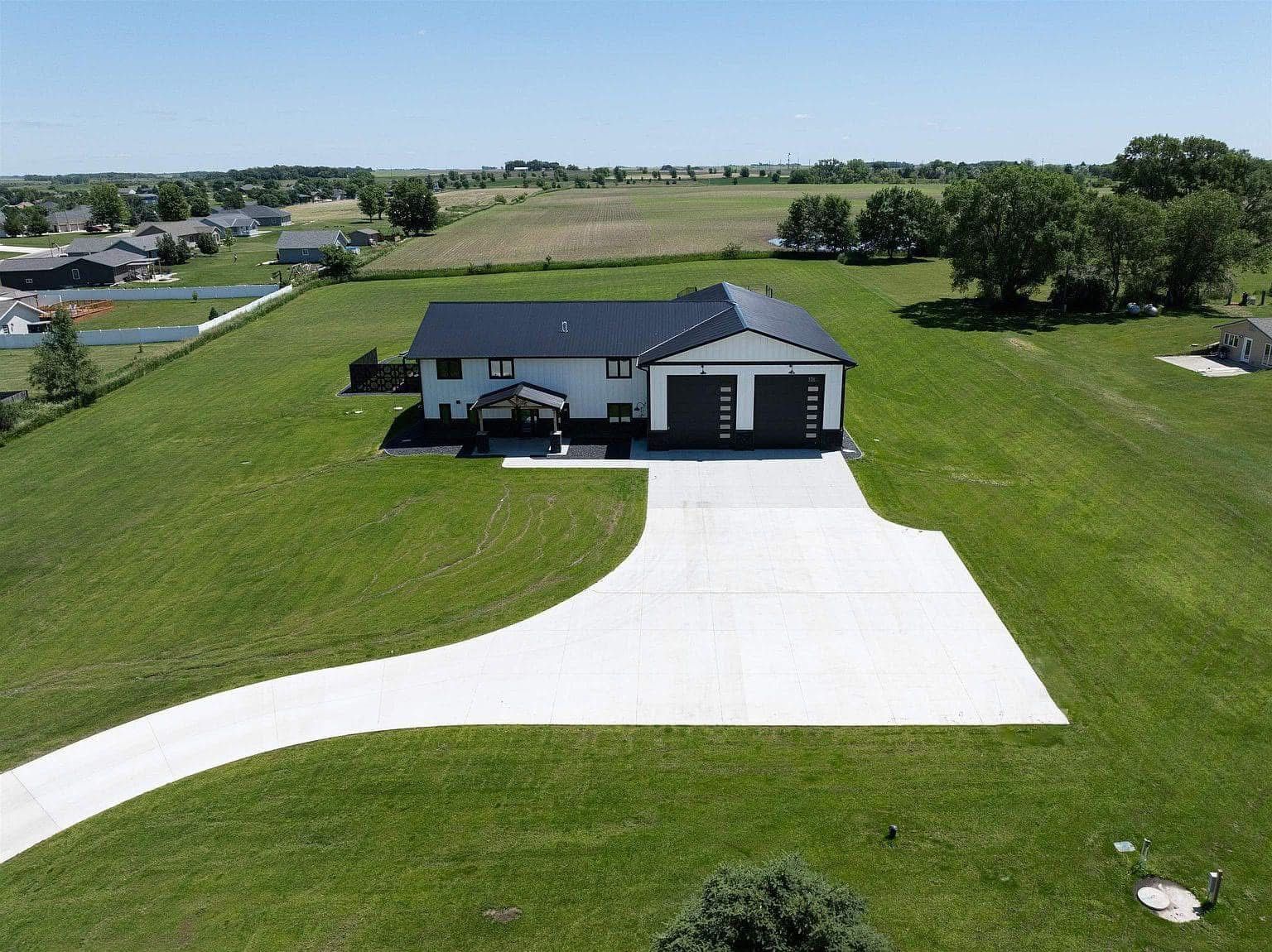 Aerial view of a single-story house with a wide white driveway and large green lawn.