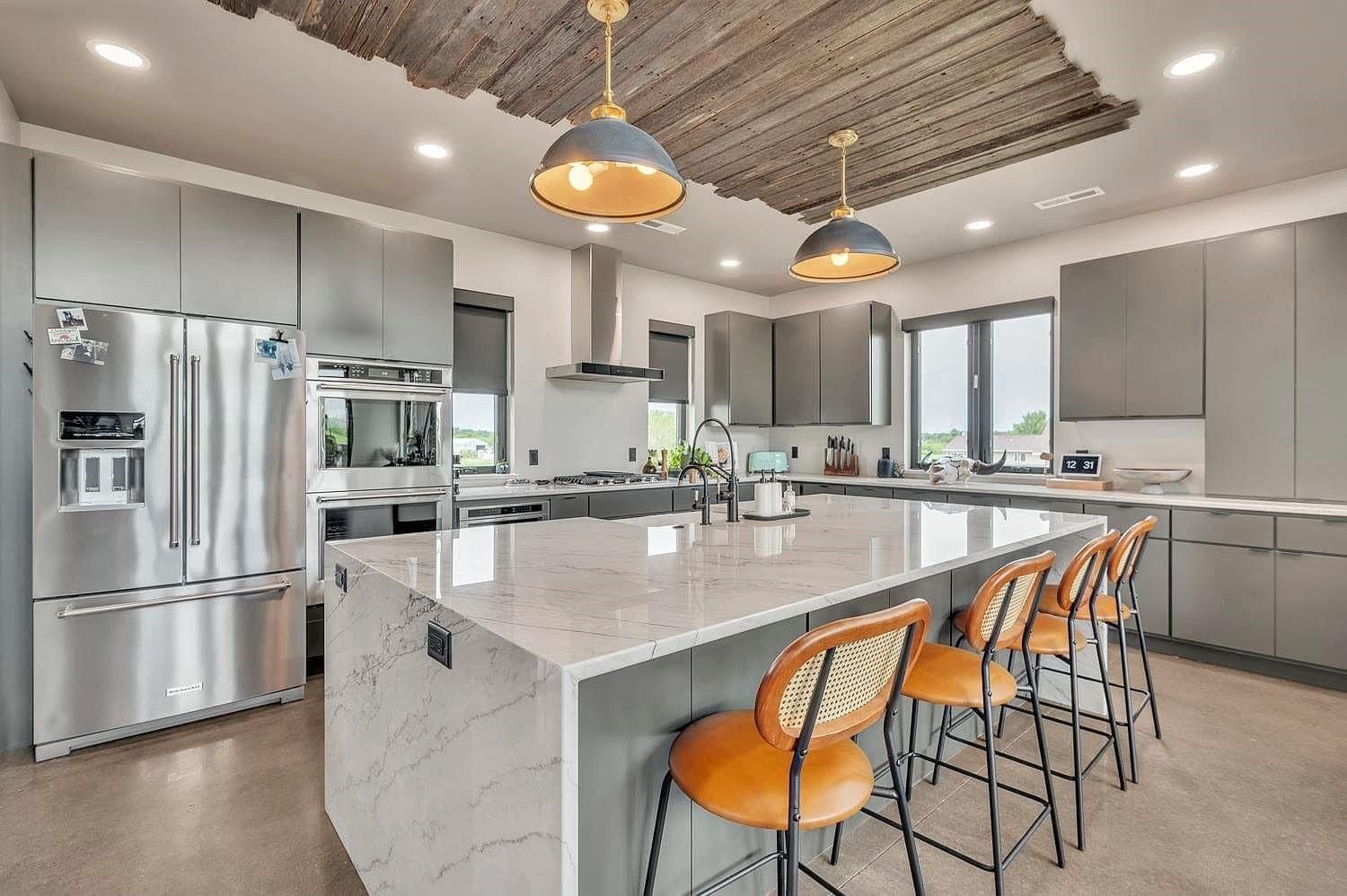 Modern kitchen with stainless steel appliances, large island, and four orange bar stools