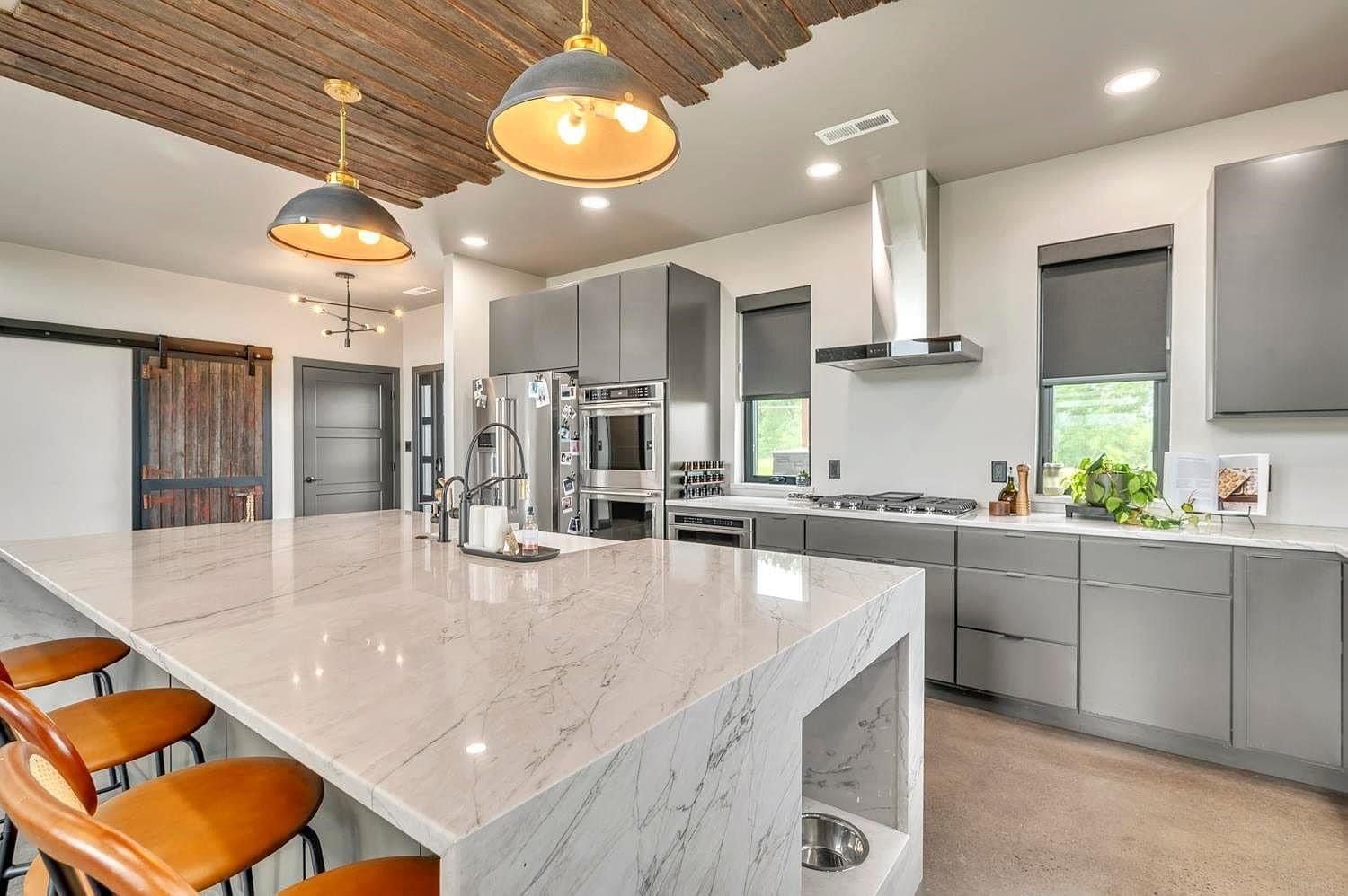 Bright modern kitchen with marble island, pendant lights, gray cabinets, and stainless steel appliances