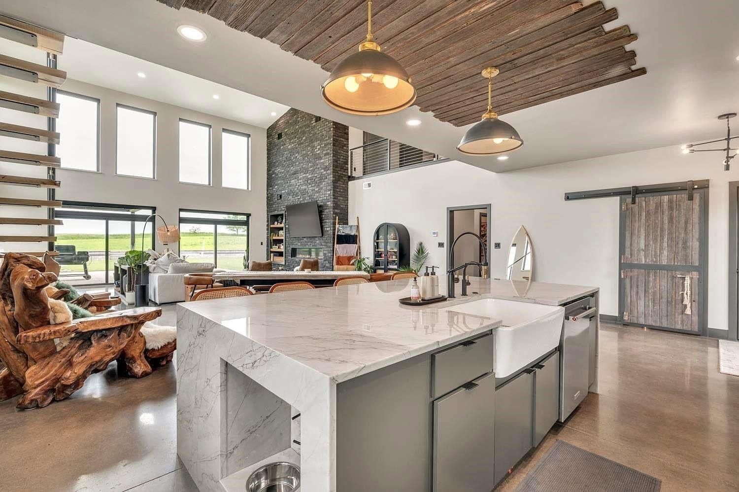 Modern kitchen with white marble island, wood ceiling beams, and large windows