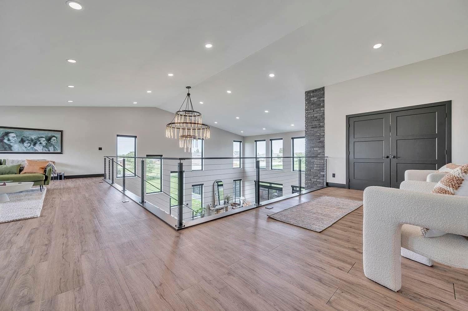 Bright open living room with wood floors, chandelier, staircase railing, and large double doors