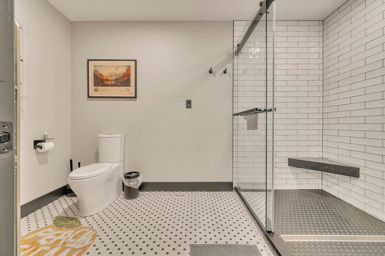 Bright bathroom with white toilet, glass shower, black-and-white tile floor, and framed wall art.