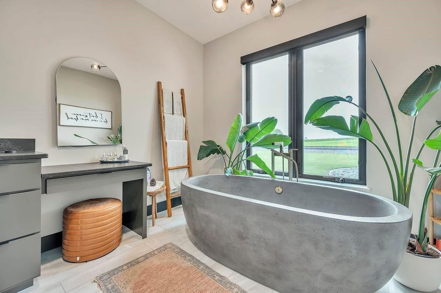 Modern bathroom with gray soaking tub, vanity, large window, plants, and woven basket stool