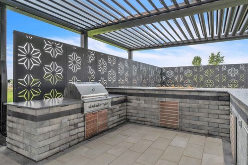 Outdoor patio with built-in gray brick grill and black patterned privacy walls under a slatted pergola