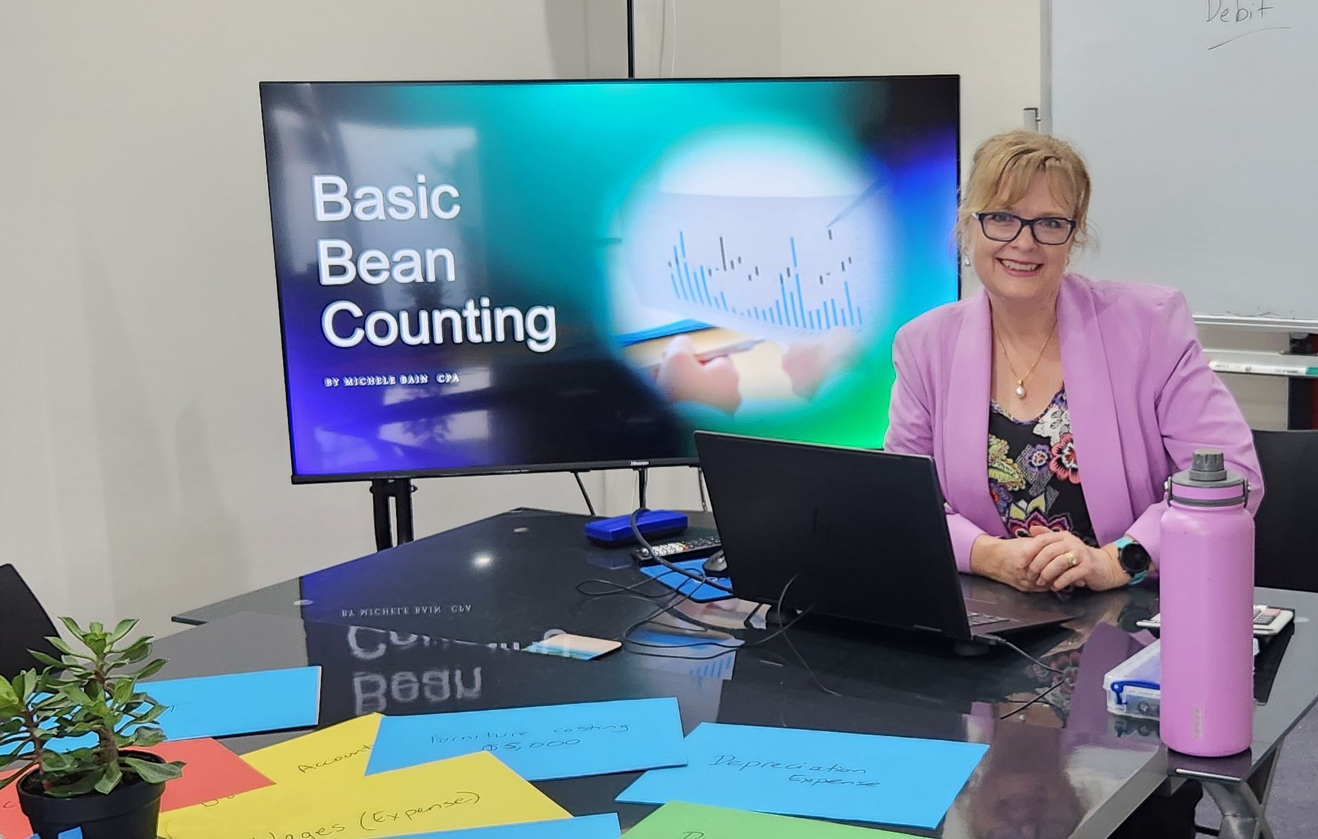 A Woman Is Sitting at A Desk Using a Laptop Computer and Writing in A Notebook — Adding Value CFO Pty Ltd in Larrakeyah, NT