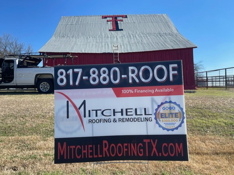 Mitchell Roofing & Remodeling sign on a red barn with phone number and website in a grassy field