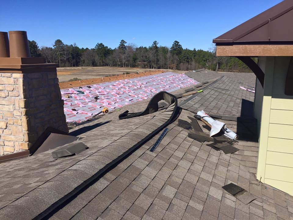 Roof with shingles being replaced, showing exposed underlayment. Chimney and trees in the background.