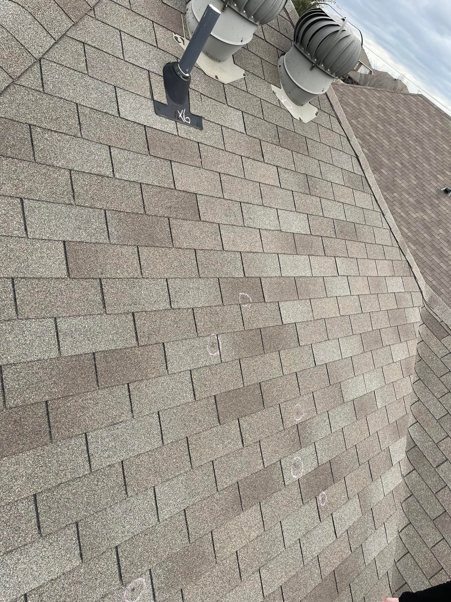 Brown asphalt shingle roof with vents and a black metal attachment. Overcast sky.