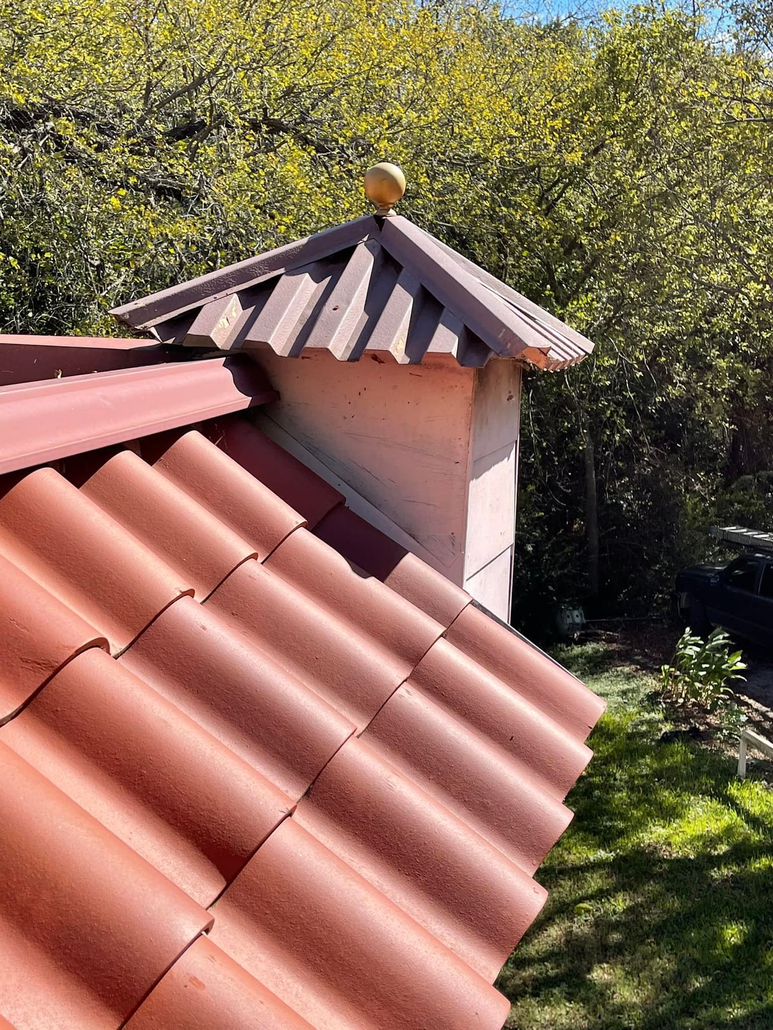 Red tile roof with a chimney topped by a golden sphere against a background of green trees.