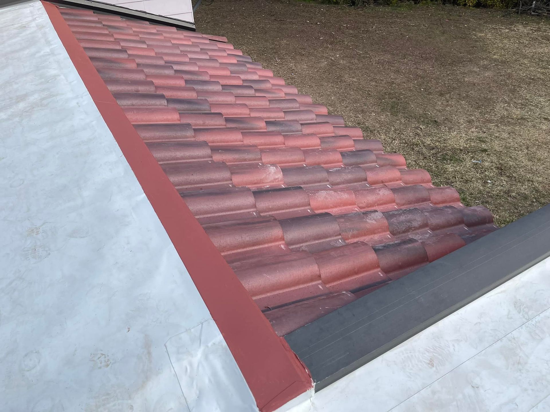 Red tile roof with red trim meets white surface and green grass.