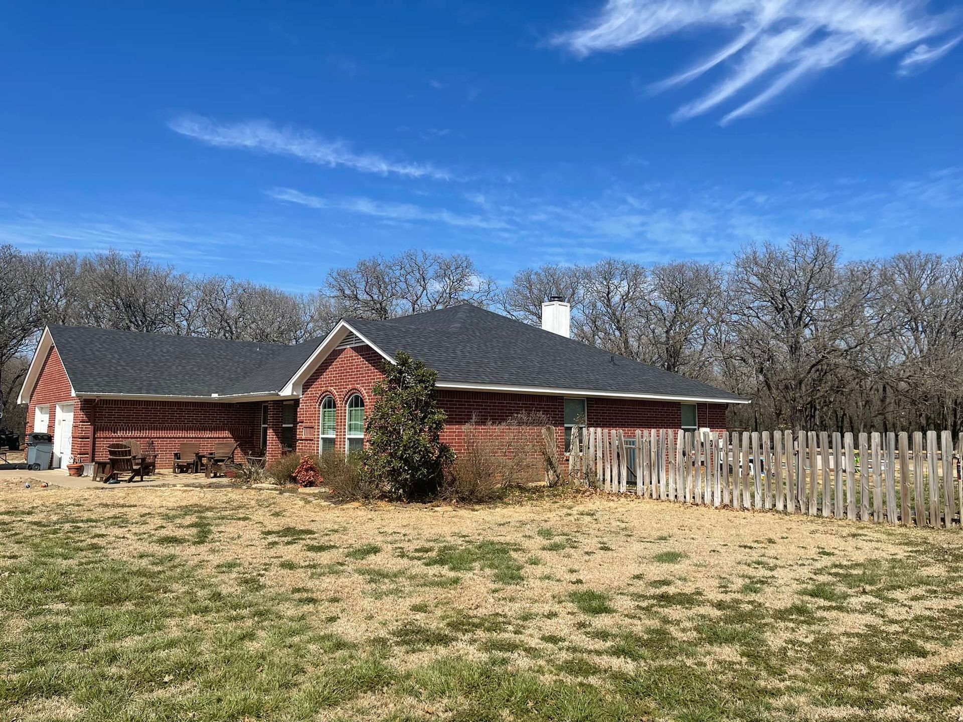 Brick house with a dark roof, white chimney, and a wooden fence on a sunny day.