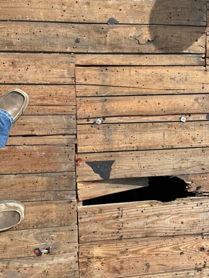 Wooden deck with missing boards and holes, with a person's feet visible.
