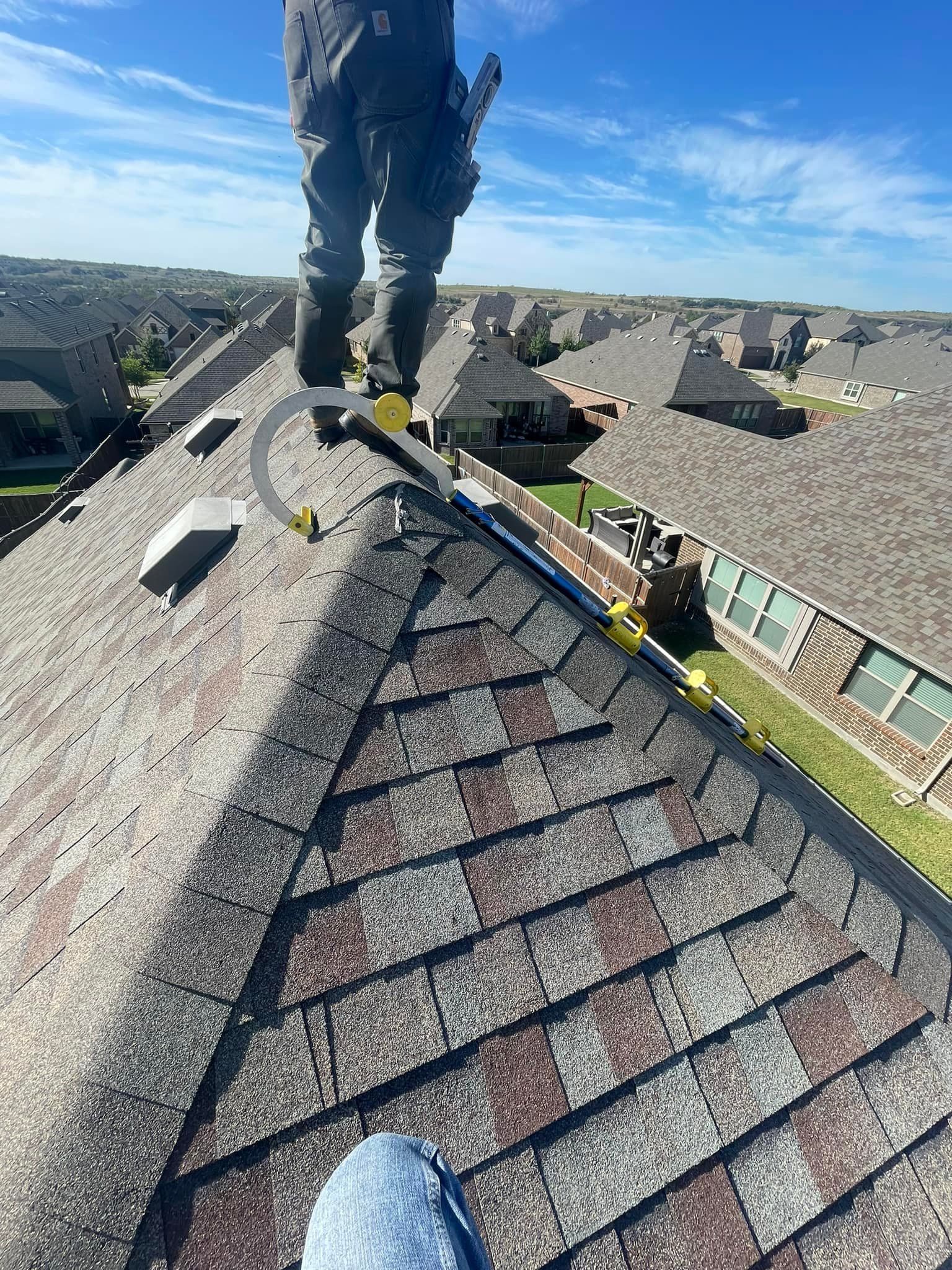 Person on a rooftop with asphalt shingles. Blue sky overhead.