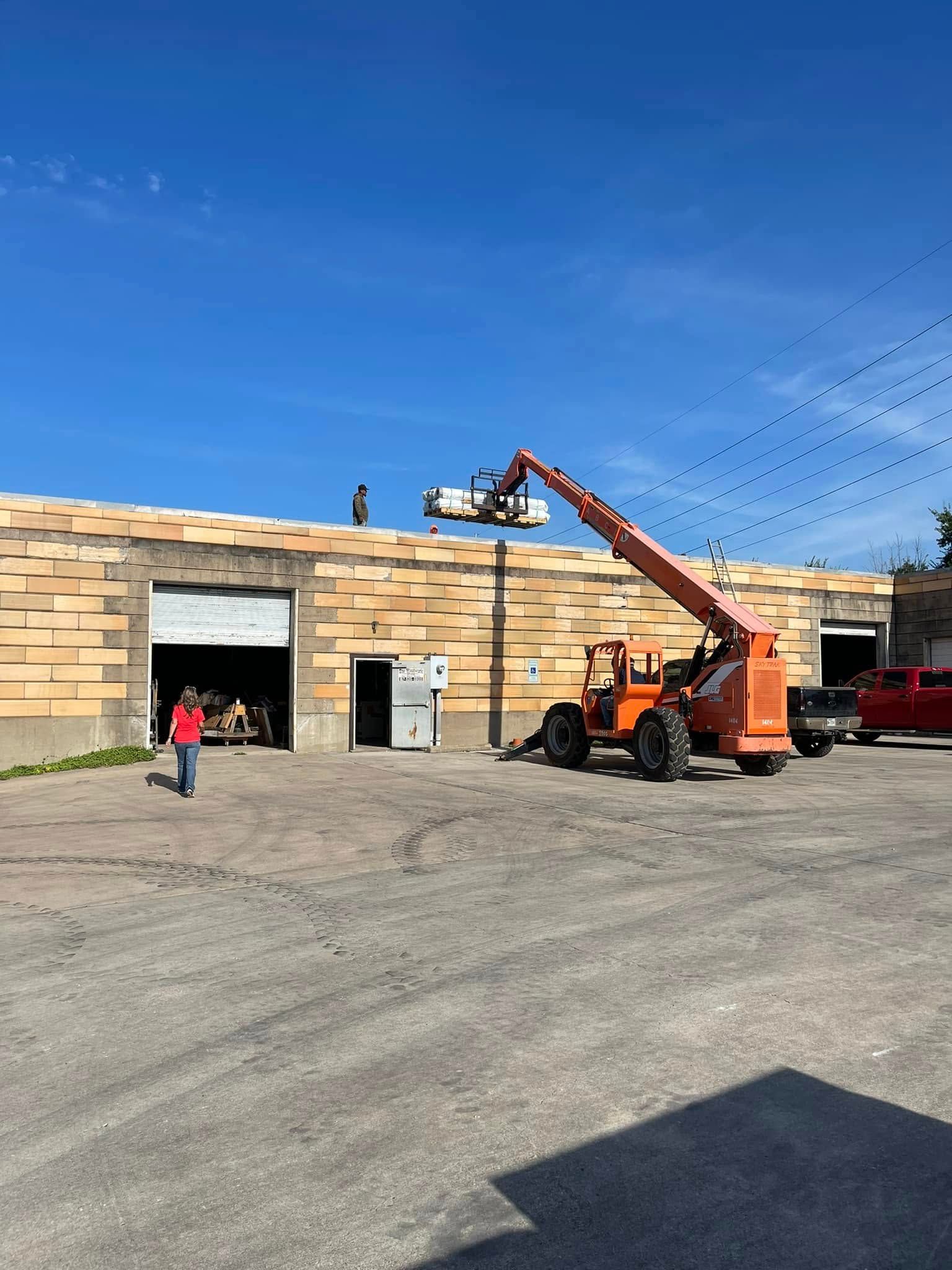 A forklift lifts materials to a roof. Workers on the roof. Blue sky. Building in a parking lot.