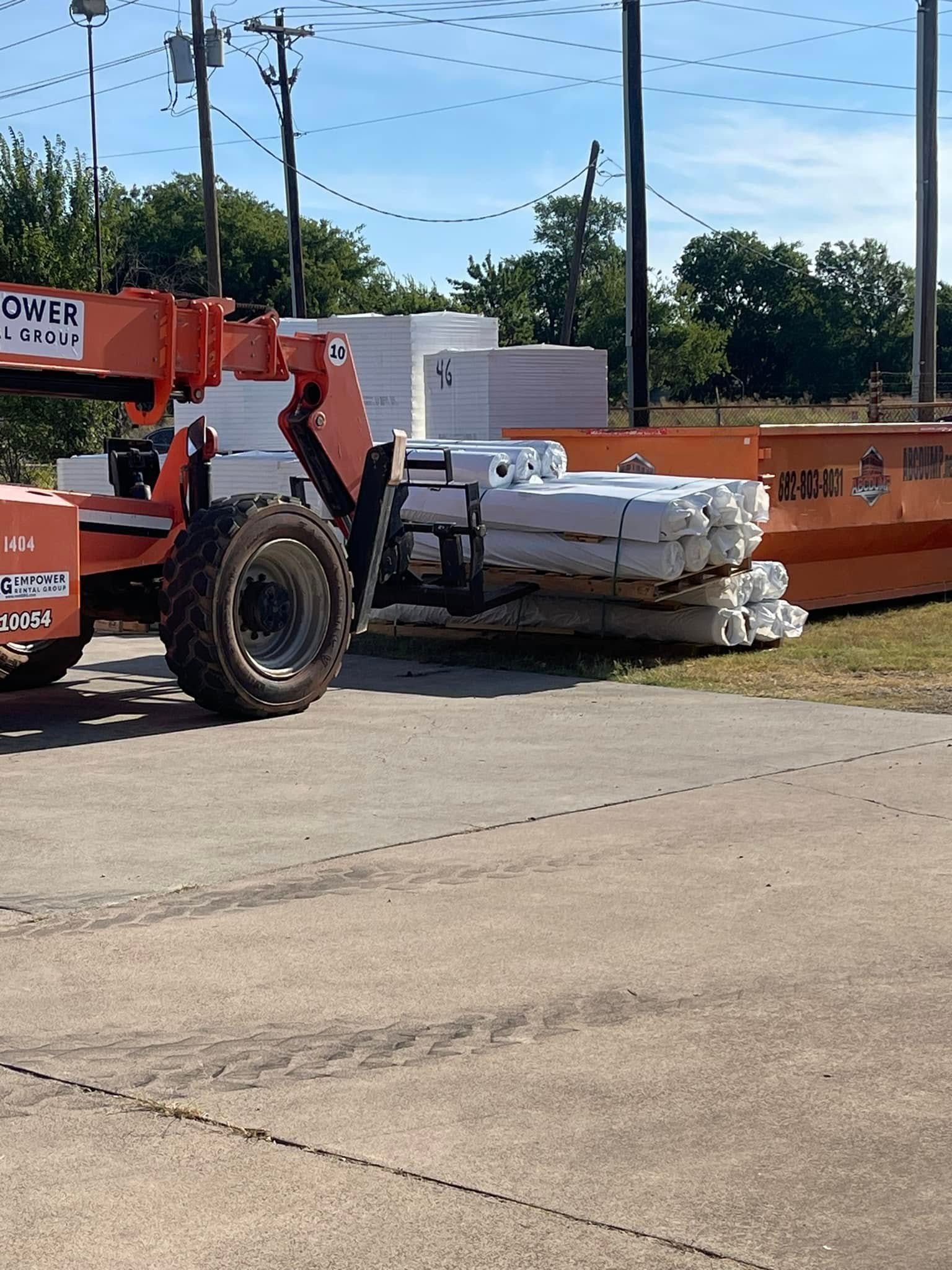 Orange forklift next to stacked white construction materials outdoors on concrete.