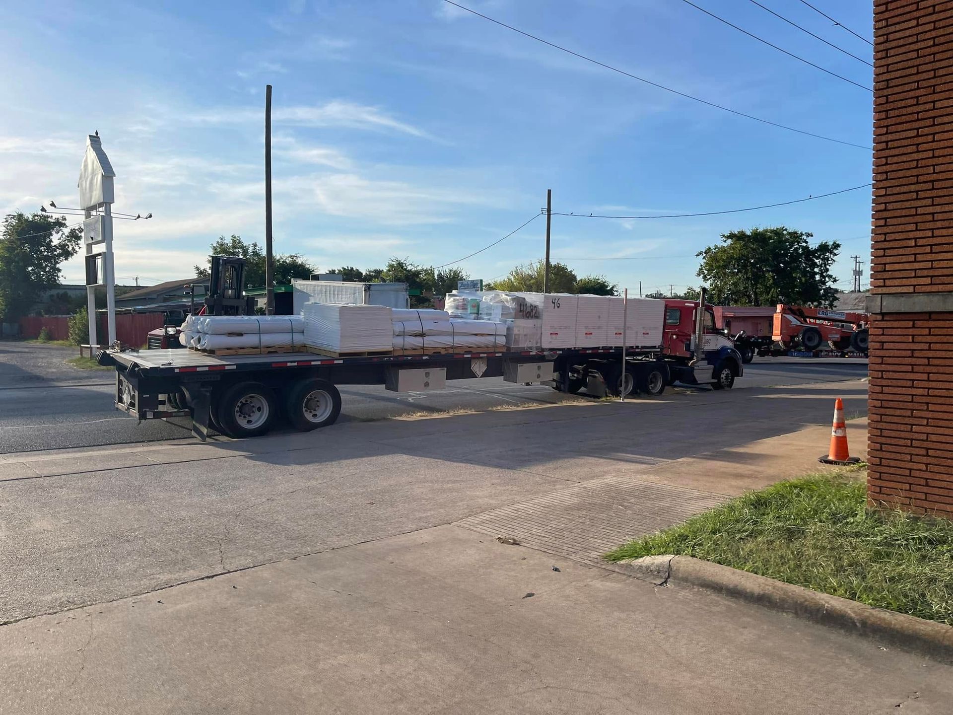 Flatbed truck loaded with construction materials parked outside brick building under blue sky.
