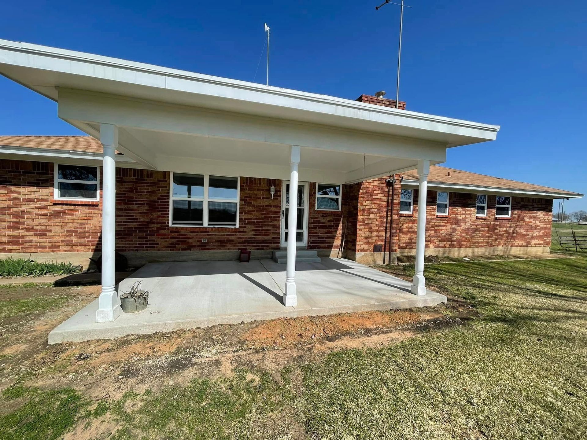 Brick house with a covered patio, white supports, concrete floor, blue sky.