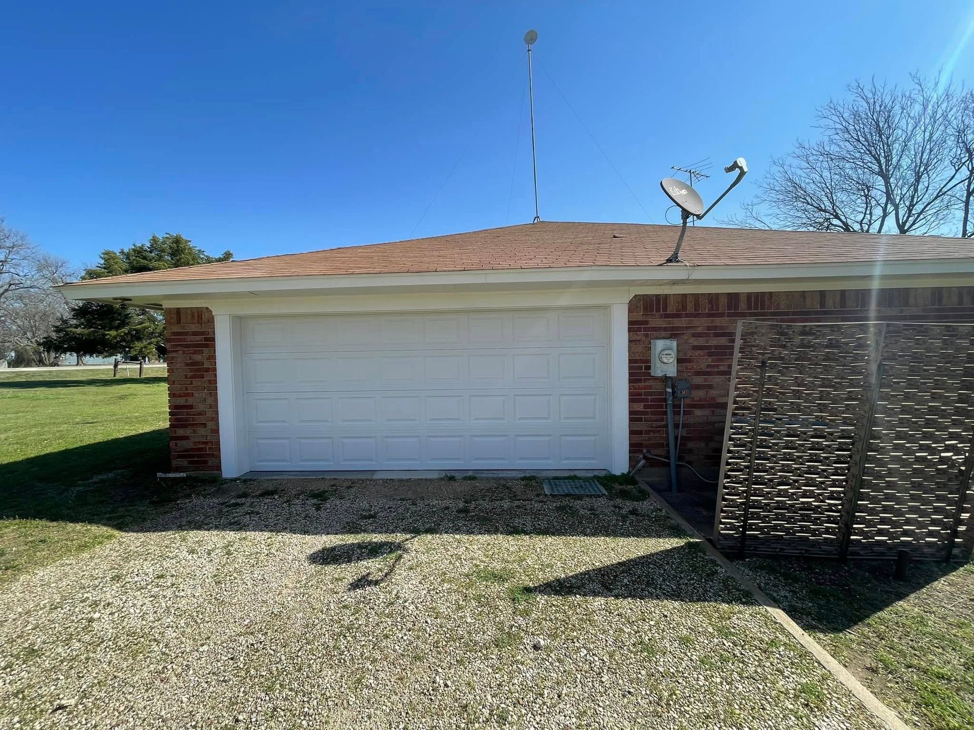 Garage with white door and red brick exterior, satellite dish on roof.