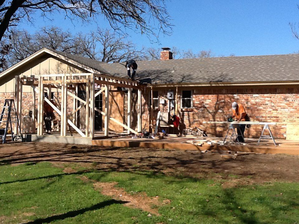 Construction workers building a wooden frame addition to a brick house on a sunny day.