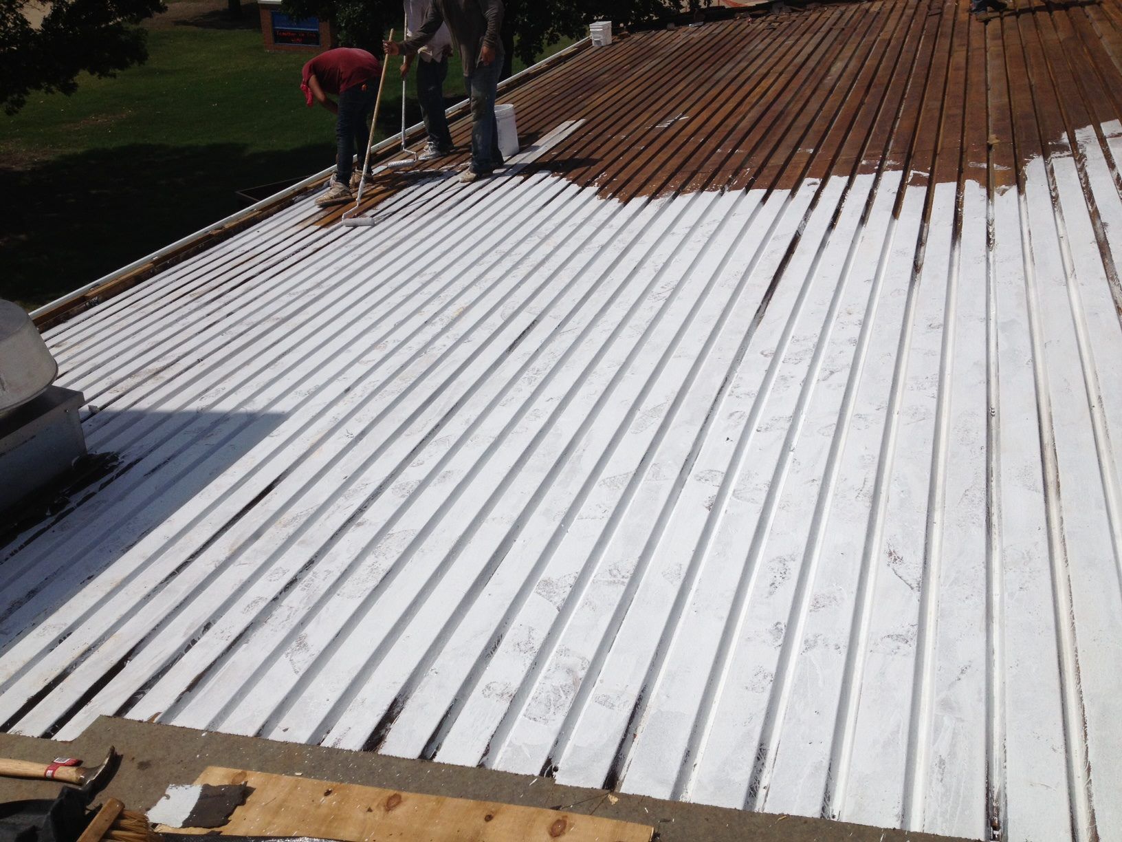People painting a corrugated metal roof white on a sunny day.