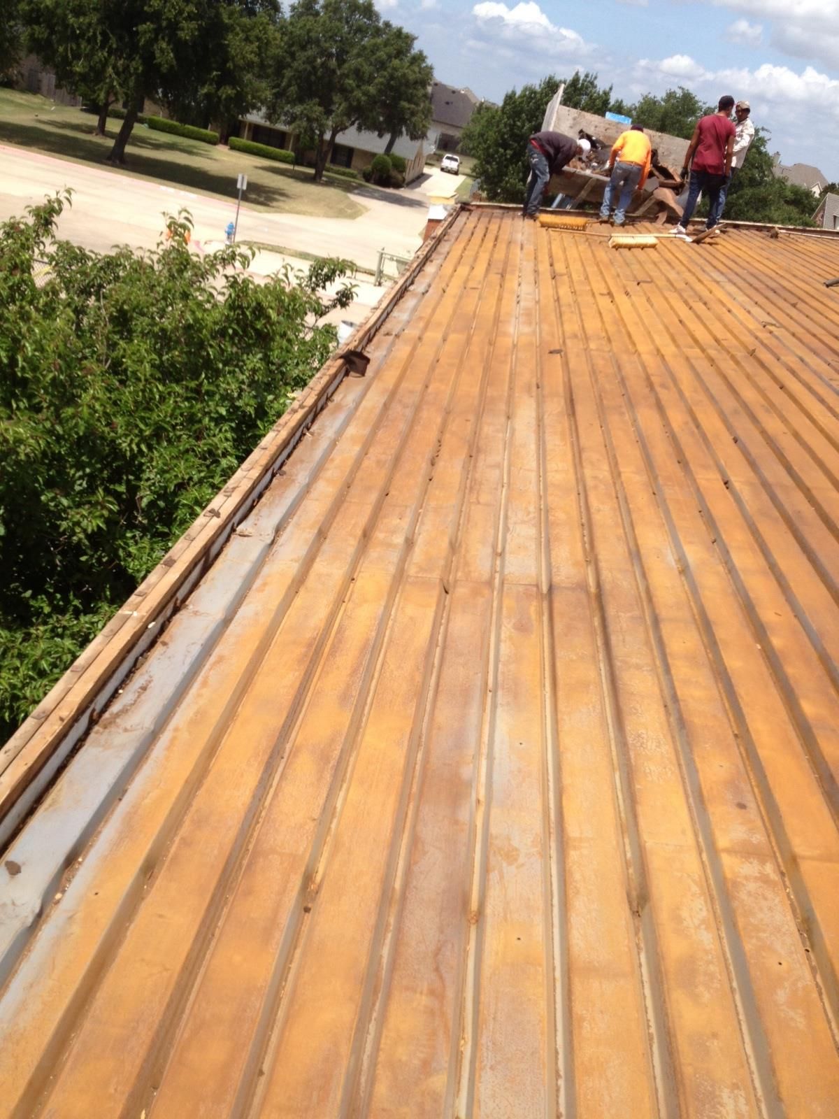 Workers on a weathered brown metal roof, preparing repairs on a sunny day.