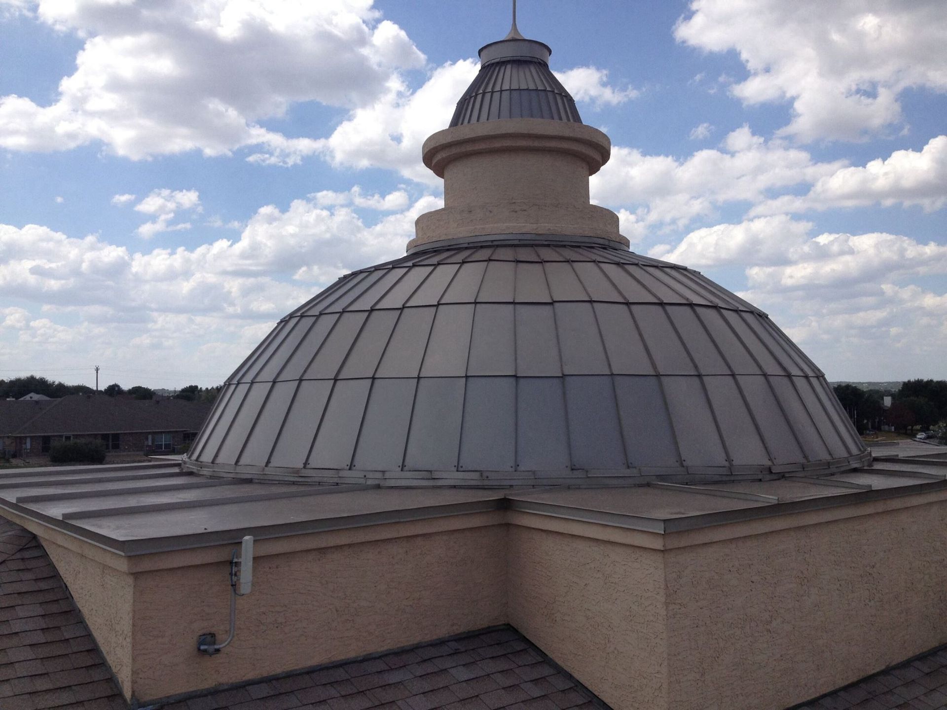Dome-shaped roof with metal panels on a building. Sky with clouds in the background.