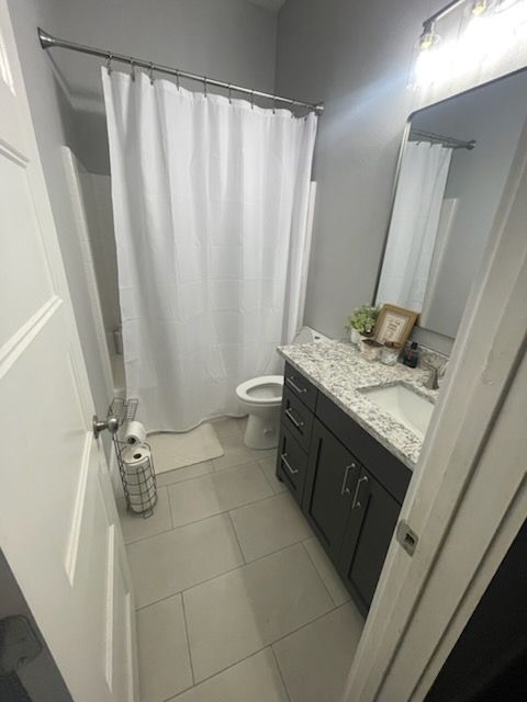 Small bathroom with gray tile, dark vanity, white shower curtain, and mirror above the sink.