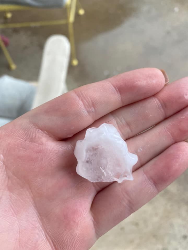 A person's hand holds a large, irregular-shaped hailstone, outdoors.