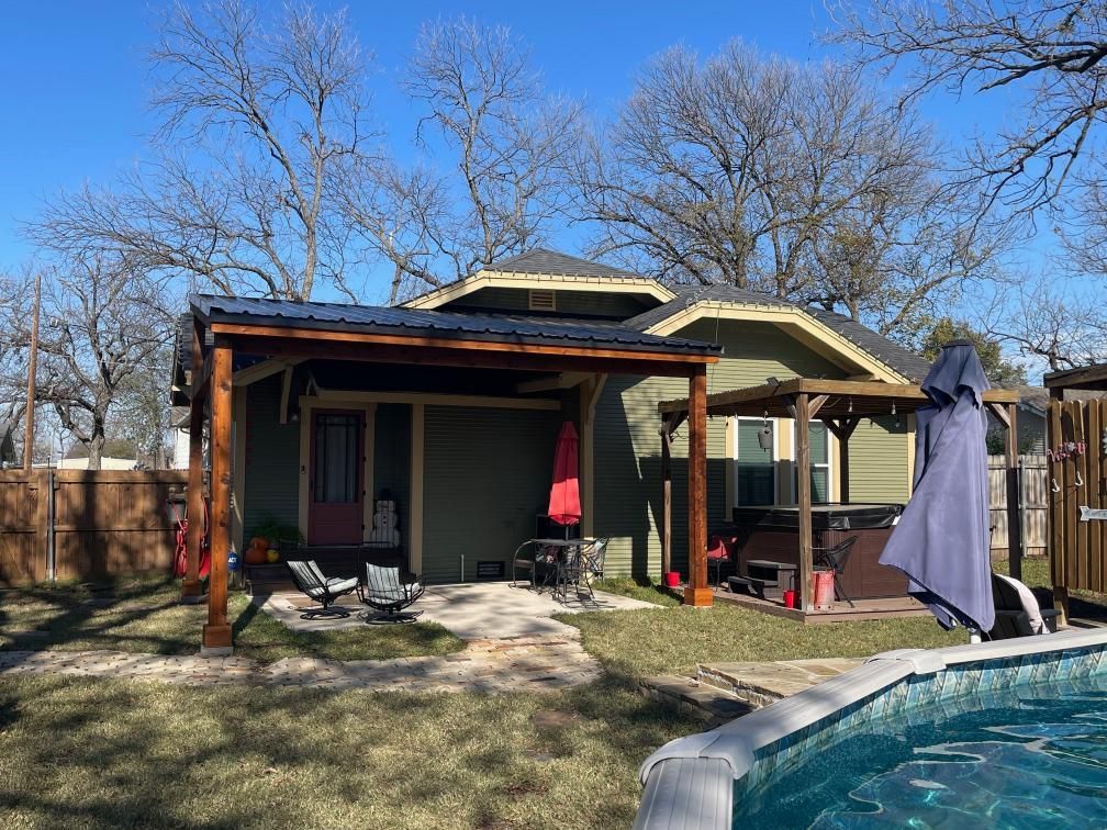 Backyard patio with a covered porch, lawn, trees, and a clothesline under a clear blue sky