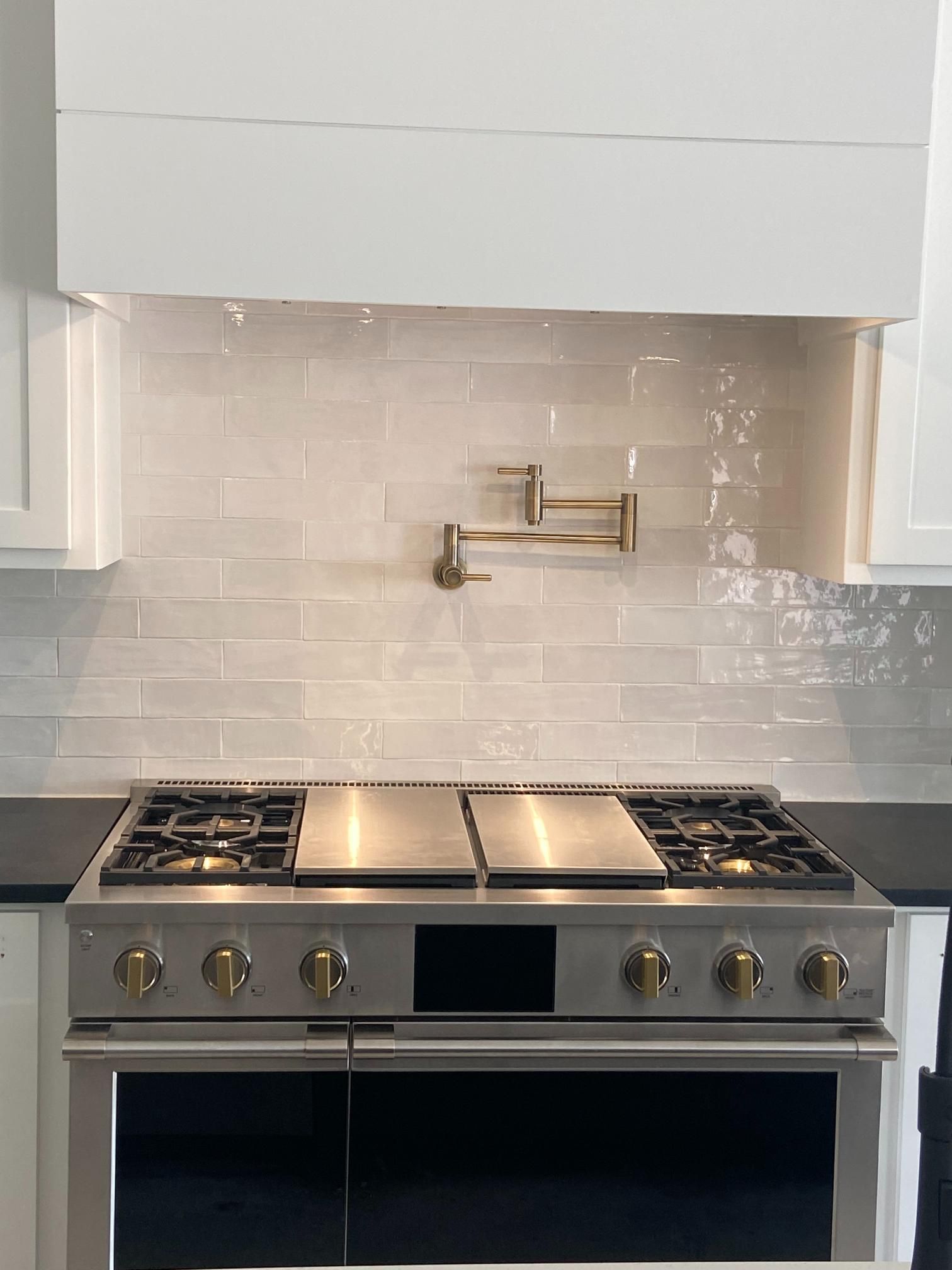 Stainless steel range beneath a white tiled backsplash and small brass pot filler in a modern kitchen