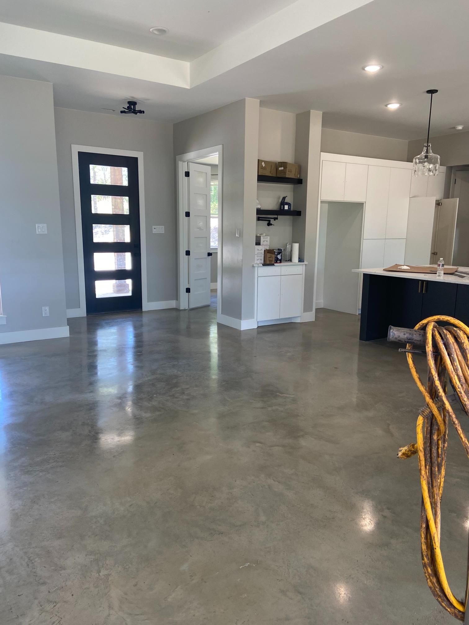 Empty modern kitchen and living area with polished concrete floor, white cabinets, and dark front door