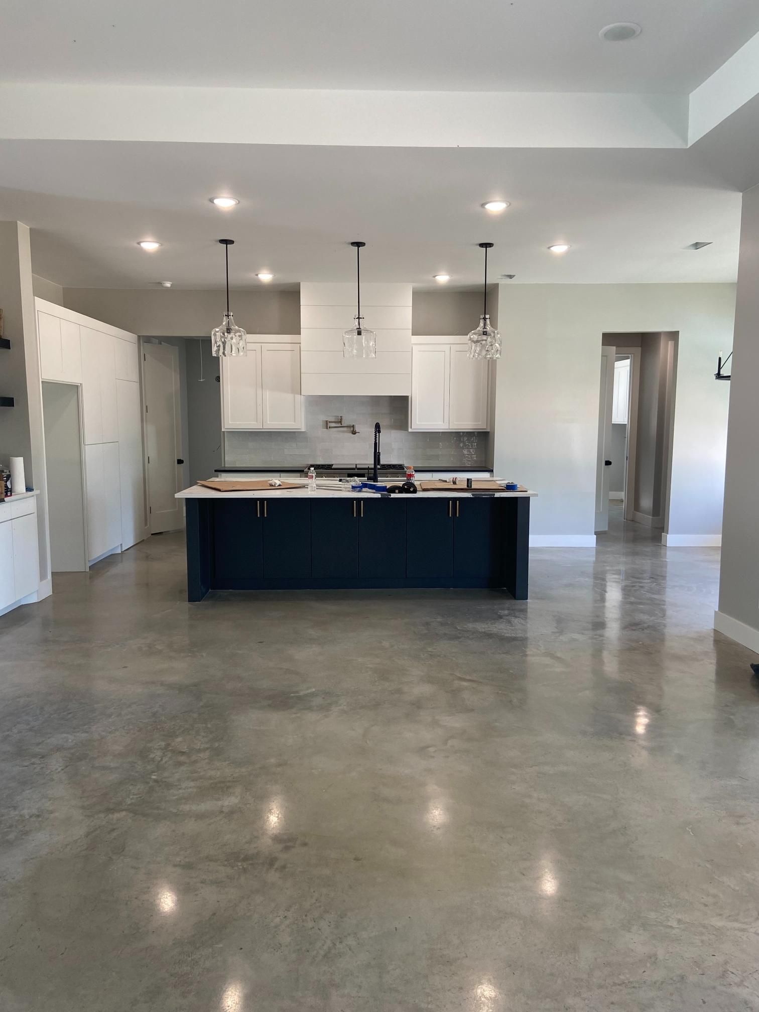 Modern open kitchen with dark island, white cabinets, concrete floor, and pendant lights