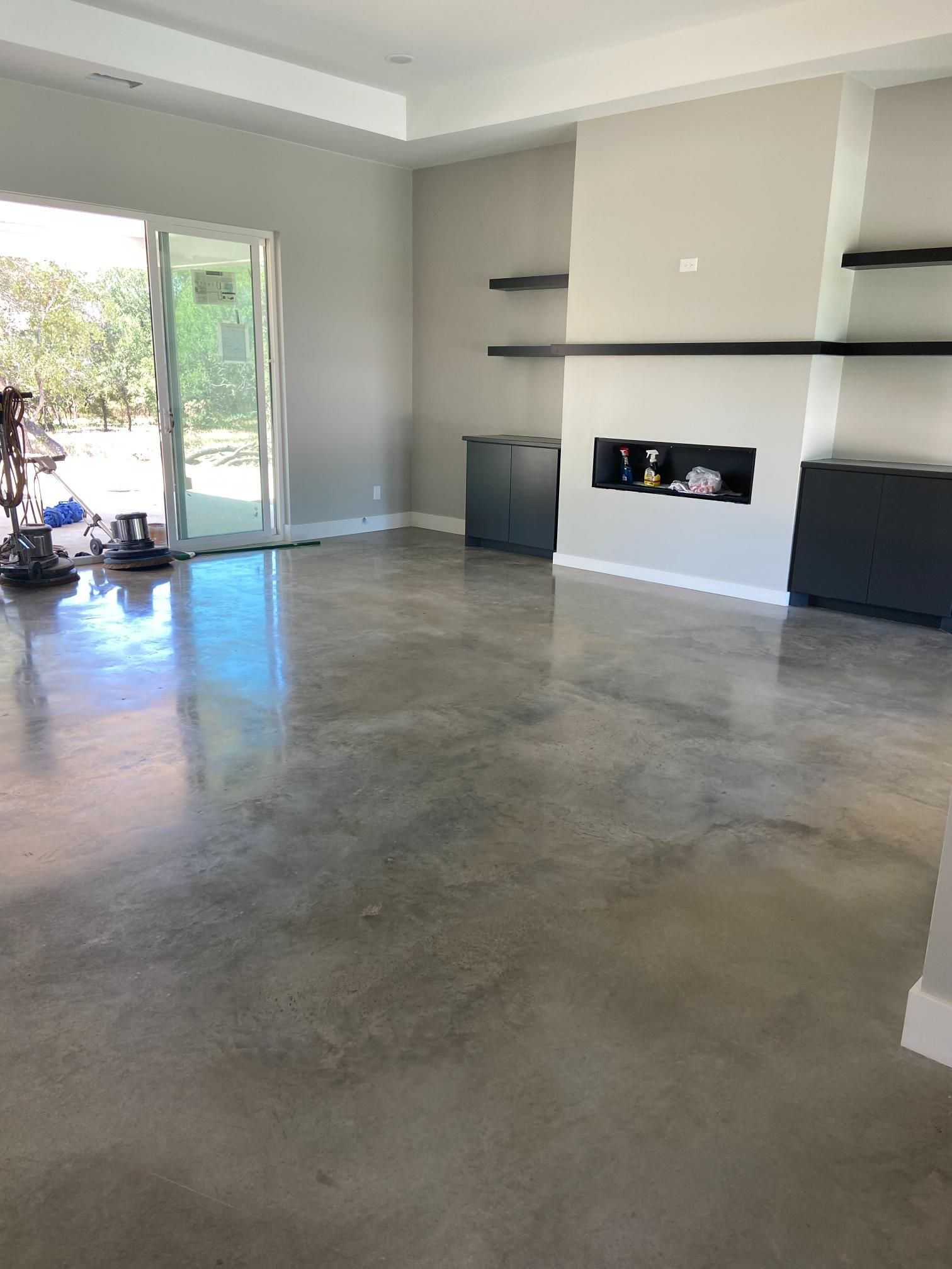 Empty modern living room with polished concrete floors, gray walls, built-in shelves, and a fireplace alcove.
