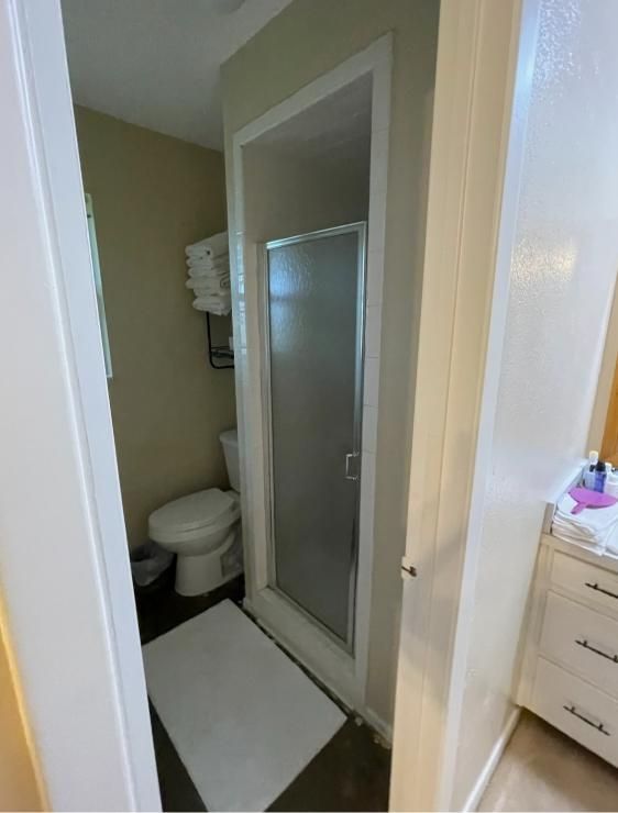 Small bathroom with shower stall, toilet, and white vanity viewed through an open doorway.