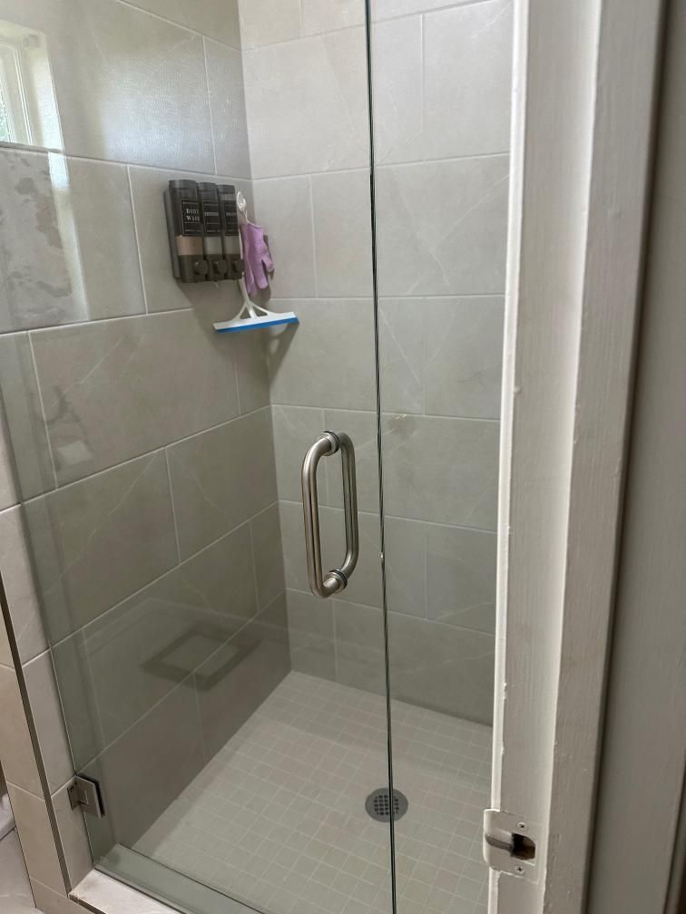 Glass shower stall with white tile walls, chrome handle, and wall-mounted soap caddy