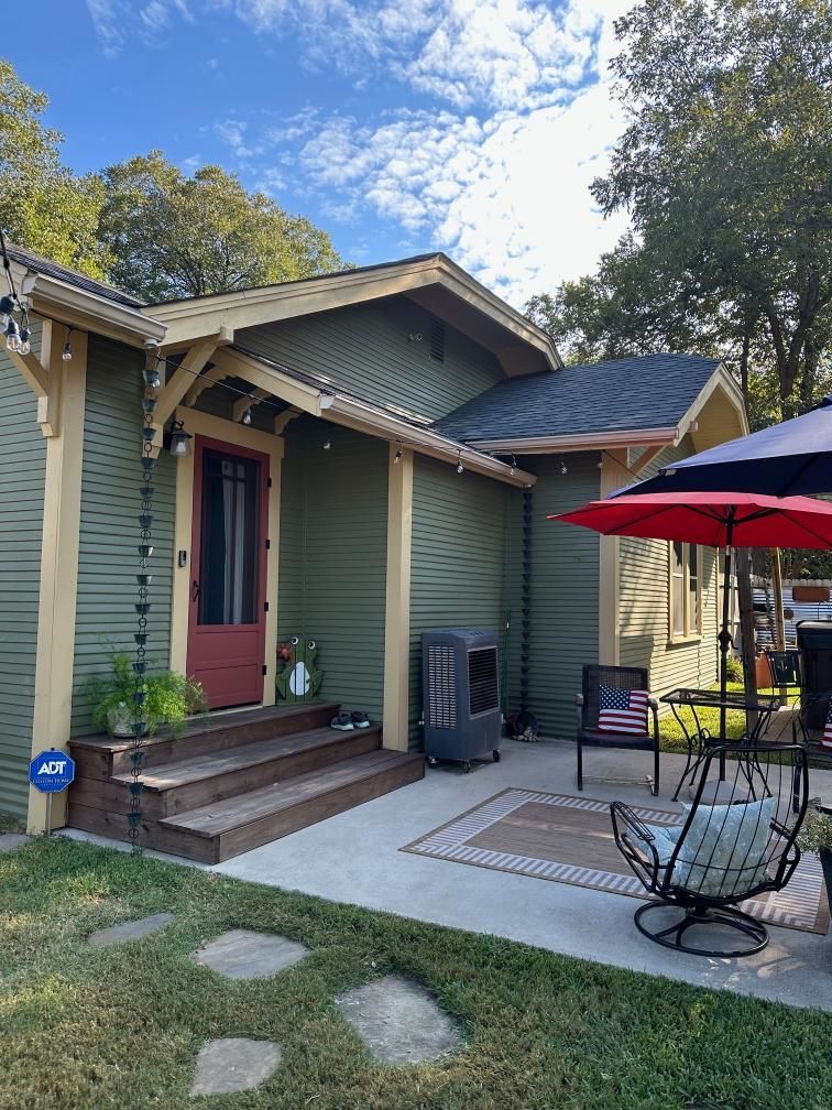 Green house entrance with steps, patio chairs, and red umbrella under a blue sky