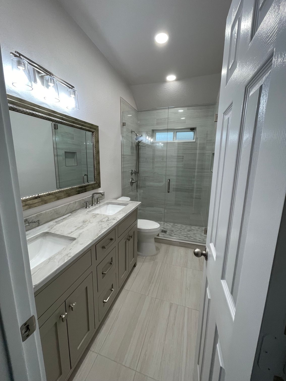 Modern bathroom with double vanity, large mirror, glass shower, and gray cabinetry
