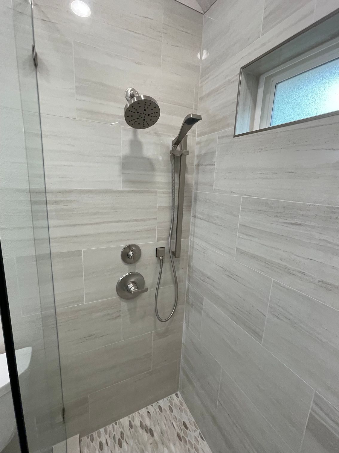 Modern tiled shower with rainfall showerhead, handheld sprayer, and window above.