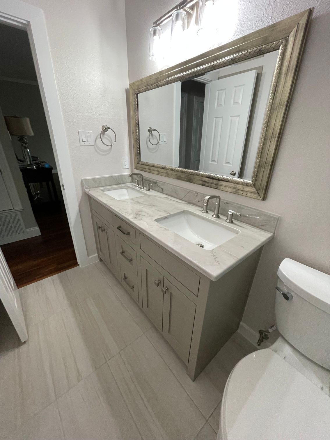 Bathroom vanity with large mirror, light wood cabinets, and a white toilet in a bright tiled room