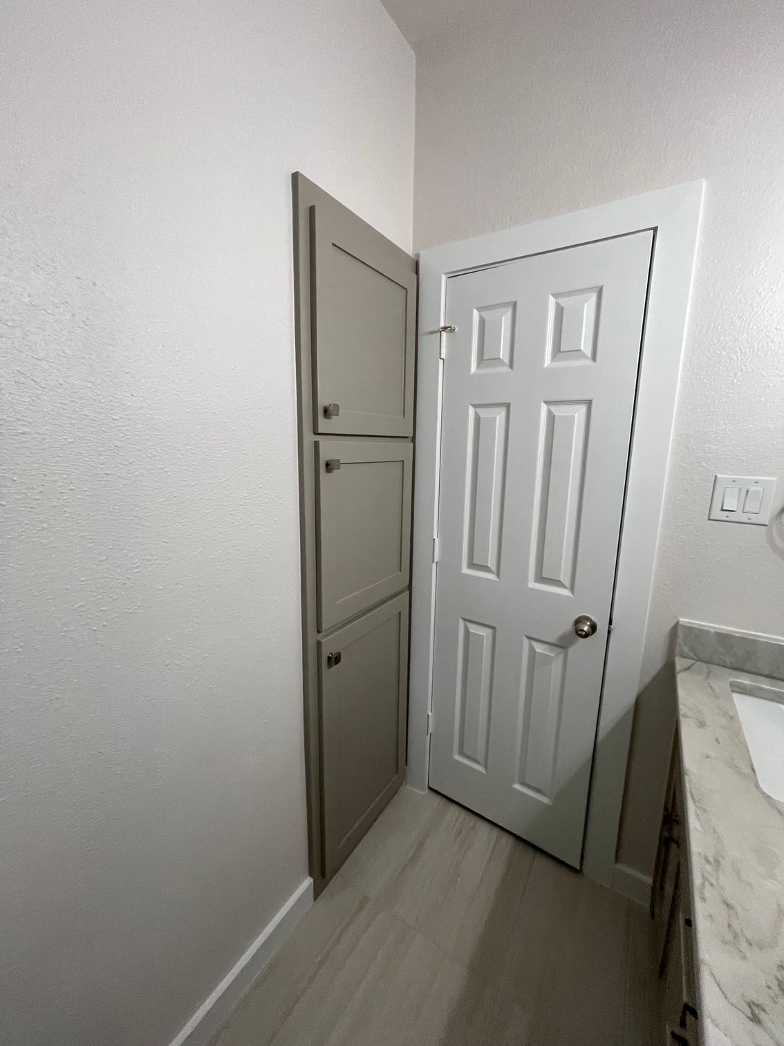 Open white door beside a gray utility cabinet in a small bathroom or laundry nook