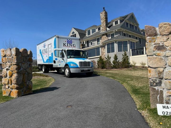 A king moving truck is parked in front of a large house.