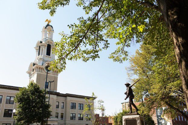 A statue of a man standing in front of a building with a clock tower in Lawrence MA