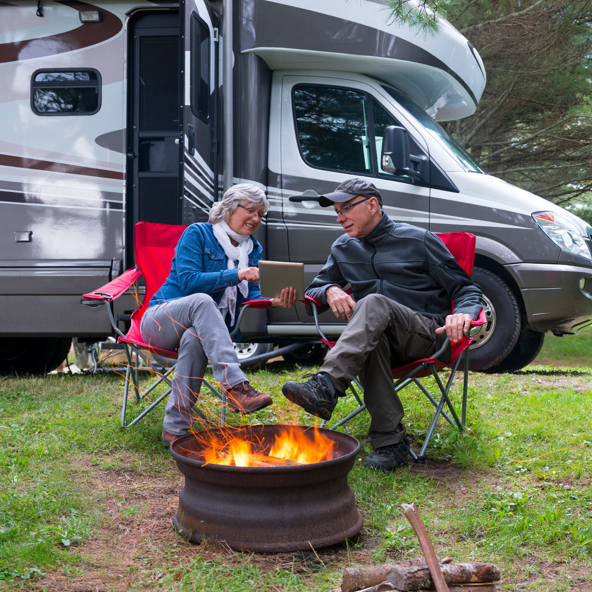 A man and a woman are sitting around a fire pit in front of a rv.