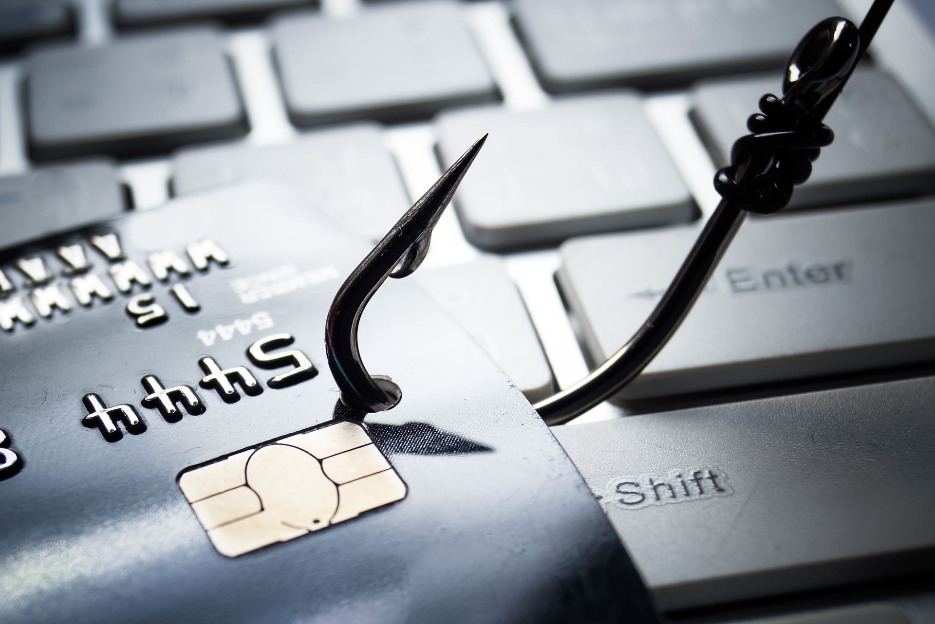 Fishing hook snags a credit card on a keyboard, symbolizing online fraud.