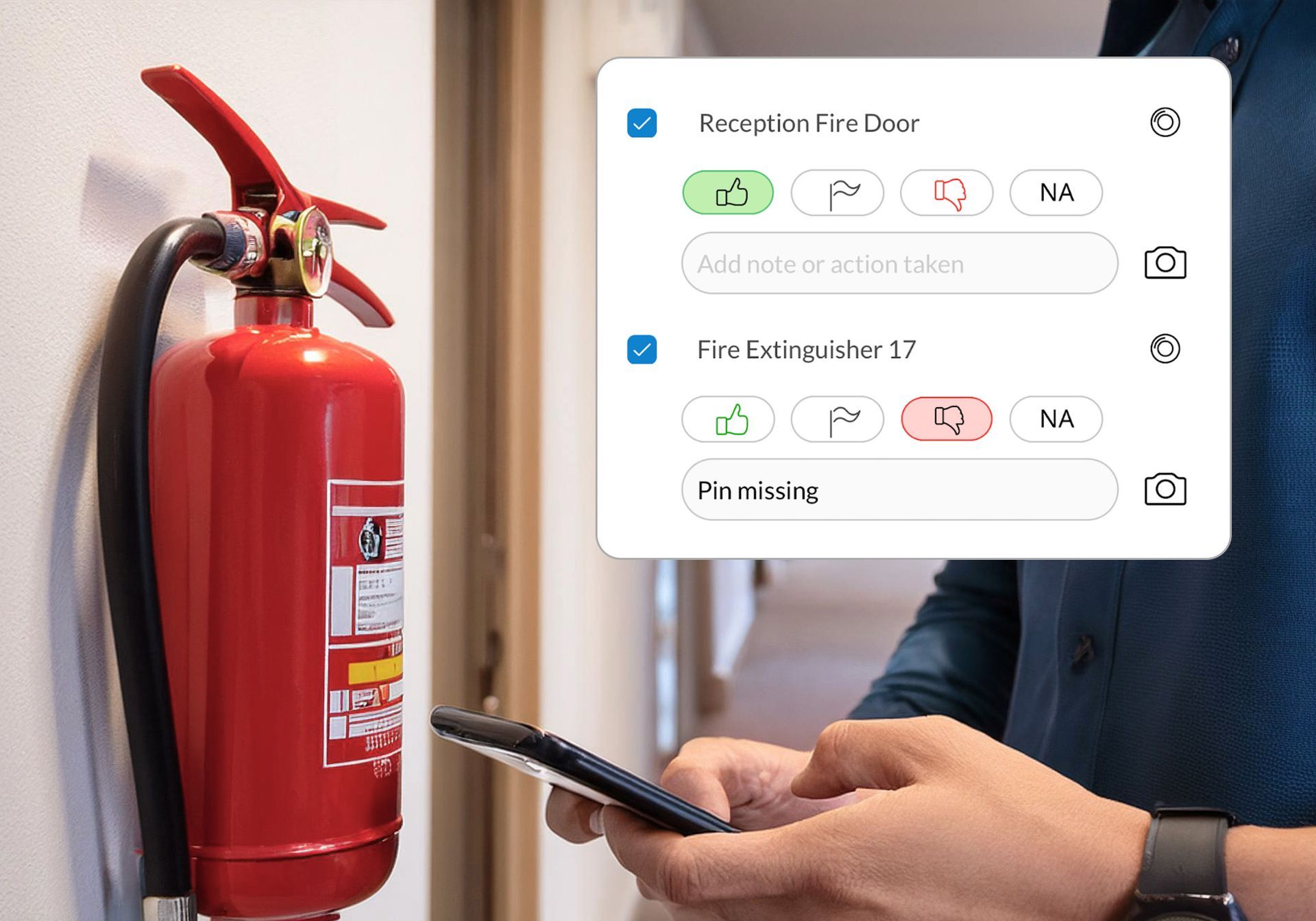 A man is holding a cell phone in front of a fire extinguisher.