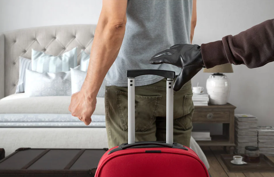 A man is standing next to a red suitcase in a bedroom.