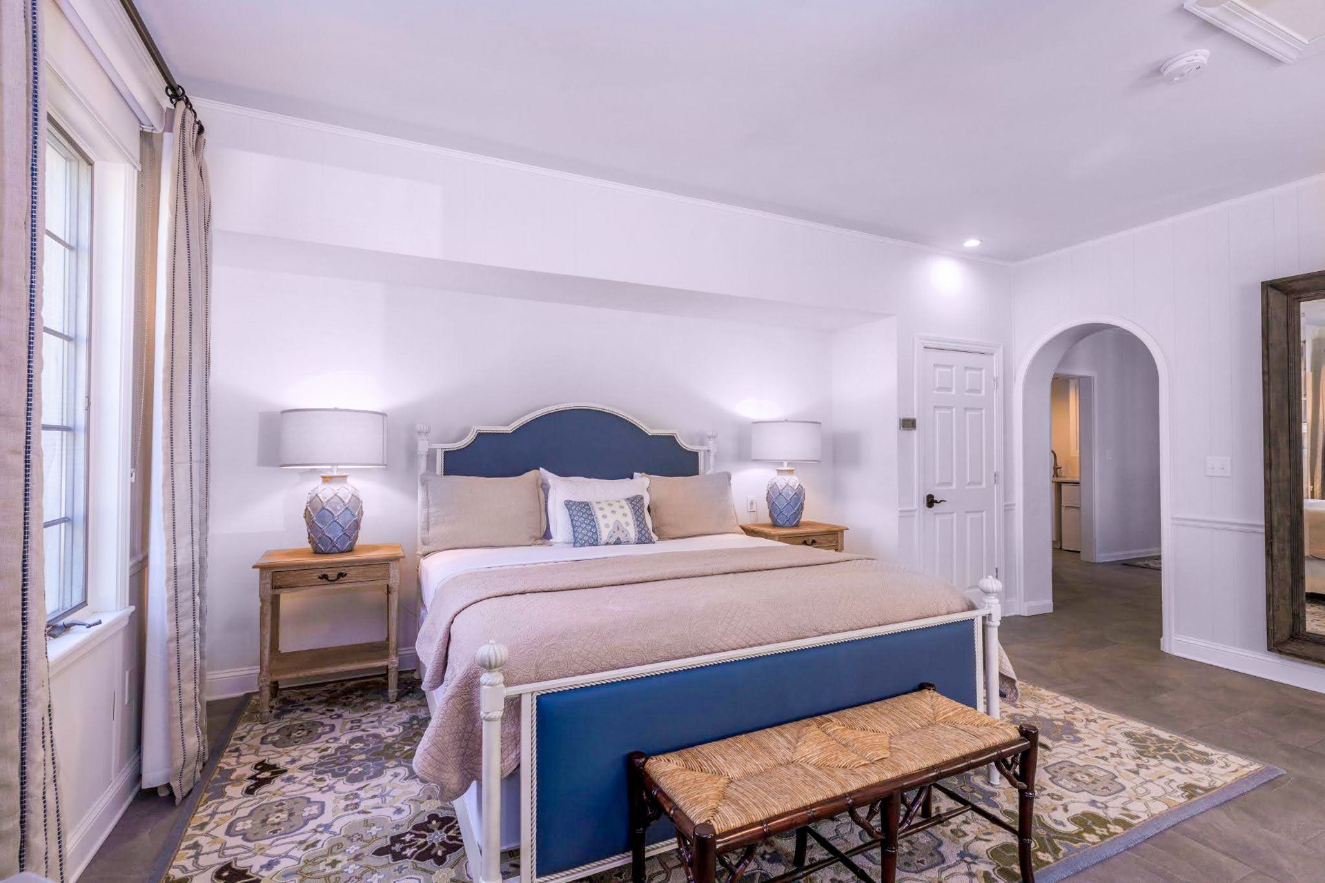 A bedroom with a king size bed , nightstands , lamps and a bench.