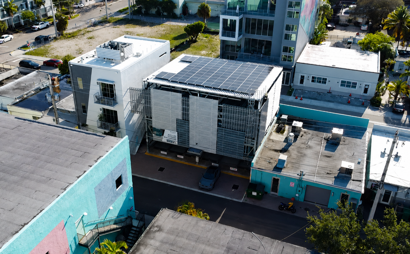 Aerial view of a small urban building with solar panels on the roof beside a turquoise building and parking lot